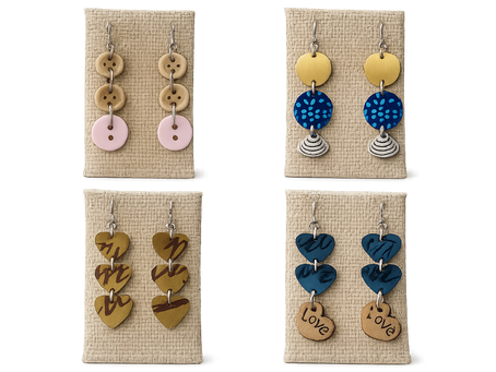 Quatre paires de boucles d'oreilles artisanales réalisées à partir de capsules Nespresso recyclées, aux motifs et couleurs variés, avec des apprêts en argent 925, présentées sur des supports en toile de jute.