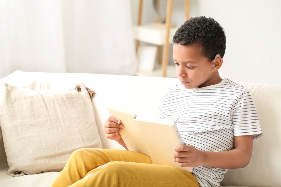 Boy with hearing aid reading book at home