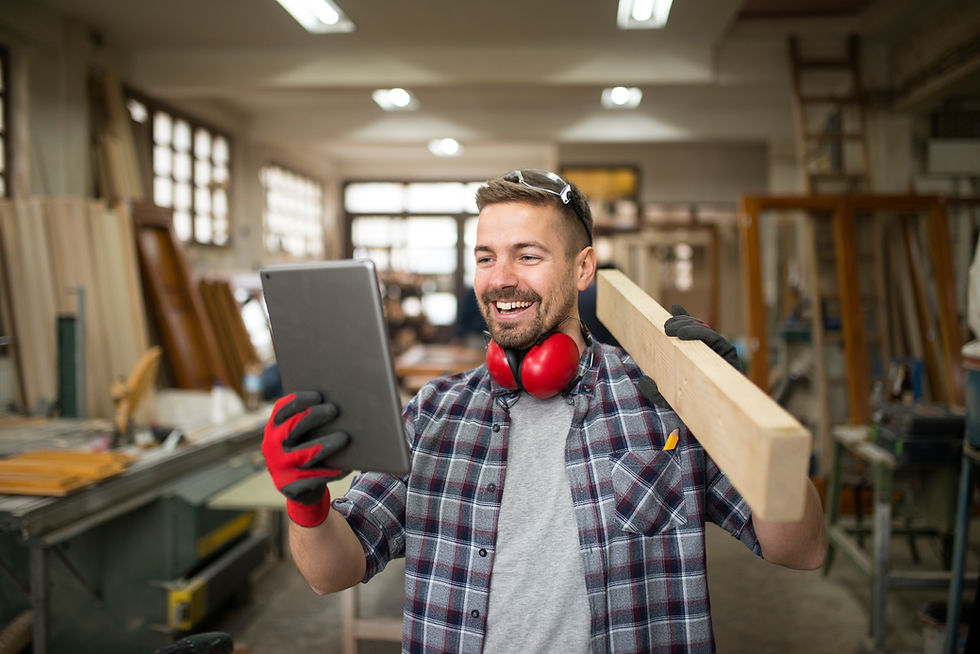 Young professional carpenter holding wood material looking at a tablet in a carpentry workshop.