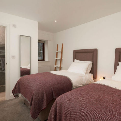 Two beds with burgundy blankets in a bright bedroom, near bathroom.