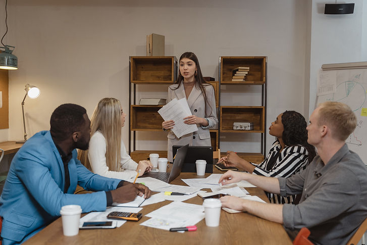 Woman leading presentation, holding papers, discussing with team members around the table