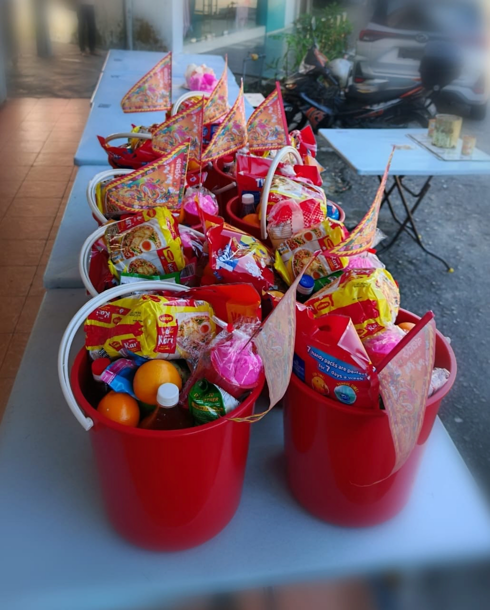 A collection of offering sets prepared in red buckets, filled with food items, drinks, fruits, and paper ritual flags. Photo credit: Jess Chuen