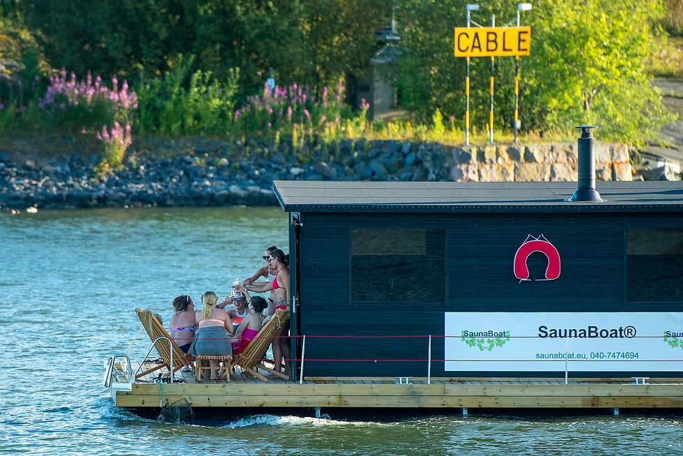 Friends enjoying a sunny day on a floating sauna boat on the river with scenic shoreline background. Helsinki, Finland. Photo by Margo Evardson.