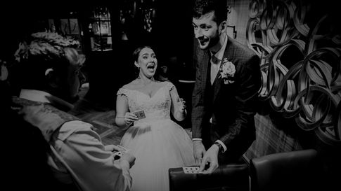 Black and white photo of a wedding magician amazing the bride and groom with a close-up card trick