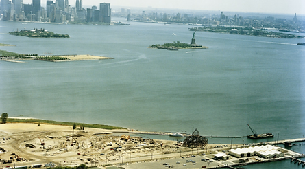 Vintage color photo taken in the 1970's showing the New York City skyline, Ellis Island and the Statue of Liberty. In the foreground is a Thalle Construction Company construction jobsite showing sitework being performed.