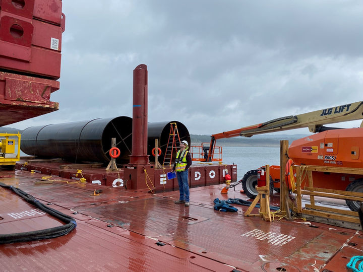 Large diameter pipes being prepared for rigging and hoisting by a large crane while floating on a barge at Lake Travis, Texas.