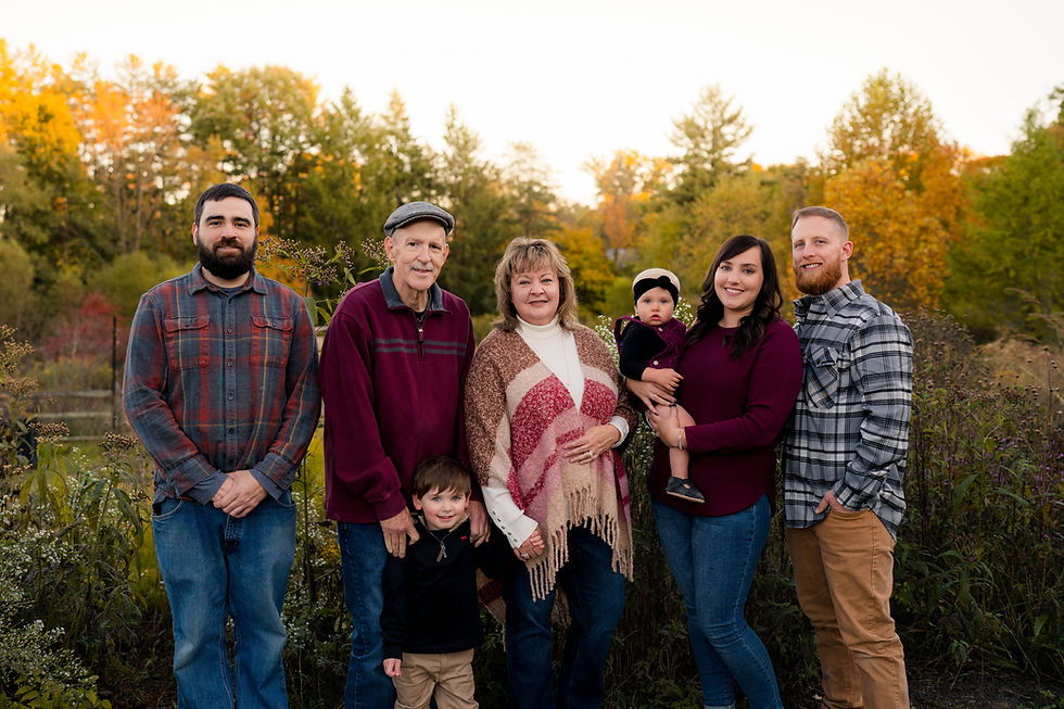 Extended family stands in front of fall foliage and smiles at the camera during family photos at the Cincinnati Nature Center in Milford, Ohio.
