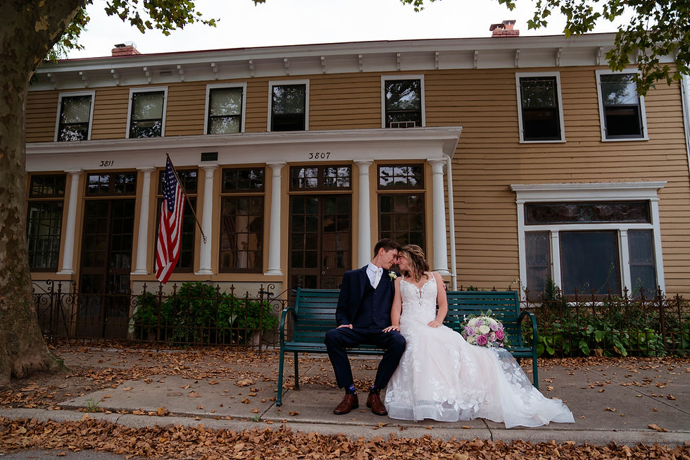 Newly married bride and groom sit together on a bench outside of The Carnegie Center of Columbia Tusculum in Cincinnati, Ohio on their October wedding day.