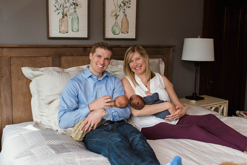 New parents sit on their bed in Cincinnati, Ohio as they hold their newborn twins and smile at the camera.