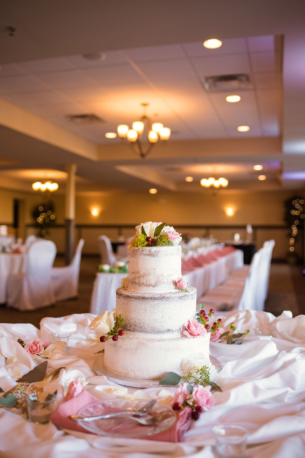 Gorgeous naked wedding cake decorated with pink and white roses and greenery sits on a table at a wedding reception in Cincinnati, Ohio.