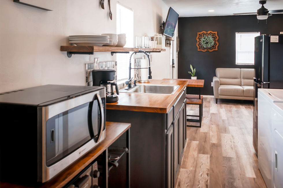 Modern kitchen with wood counters, black wall, beige chair, and microwave; cozy, tidy space with no people visible