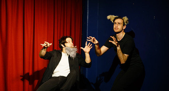 Two male actors on stage. One wears a werewolf chin, the other werewolf ears.
