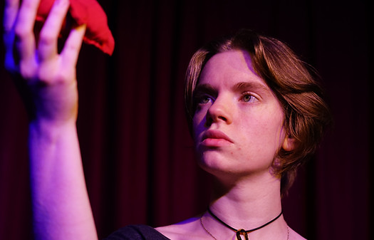 A woman sits holding a red fish in front of her. She looks at it.