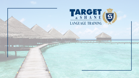 Tropikalny pomost do bungalowów nad turkusową wodą, z logo i napisem TARGET & SHANE LANGUAGE TRAINING na niebie.