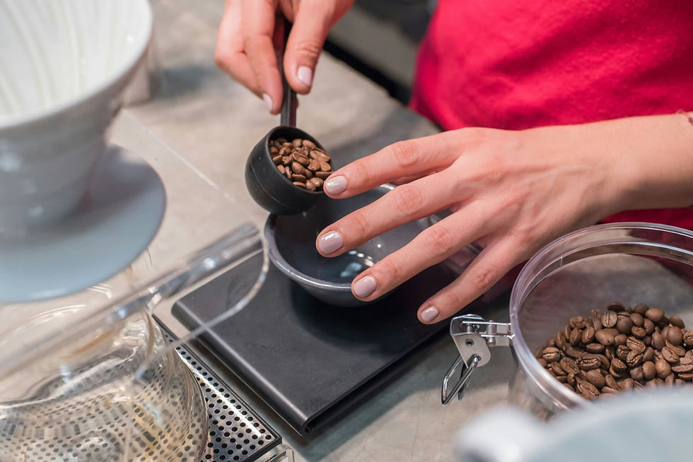 Manos miden granos de café con una cuchara sobre una báscula. Fondo de cocina, tarro y balanza visibles. Atuendo rojo. Ambiente tranquilo.