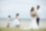 Bride and groom walking together during an intimate beach wedding, accompanied by two children and a small dog with the ocean in the background.