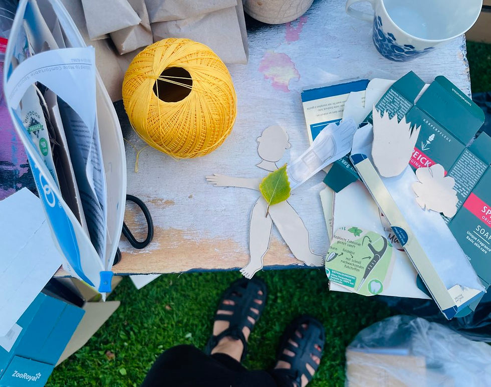 Auf einem Arbeitstisch liegen alte Verpackungen, Papierreste, ausgeschnittene Figuren, eine Schere und gelbes Garn. Keine Werbung, sondern eine kleine Auswahl der Materialien, aus denen ich am liebsten Zine-Büchlein gestalte.