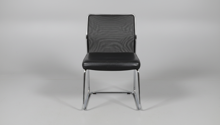 Side view of a single used visitor chair on a plain studio floor.