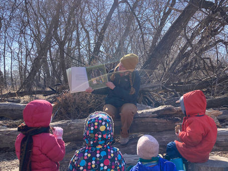 A teacher reads a storybook to four children outside in the forest