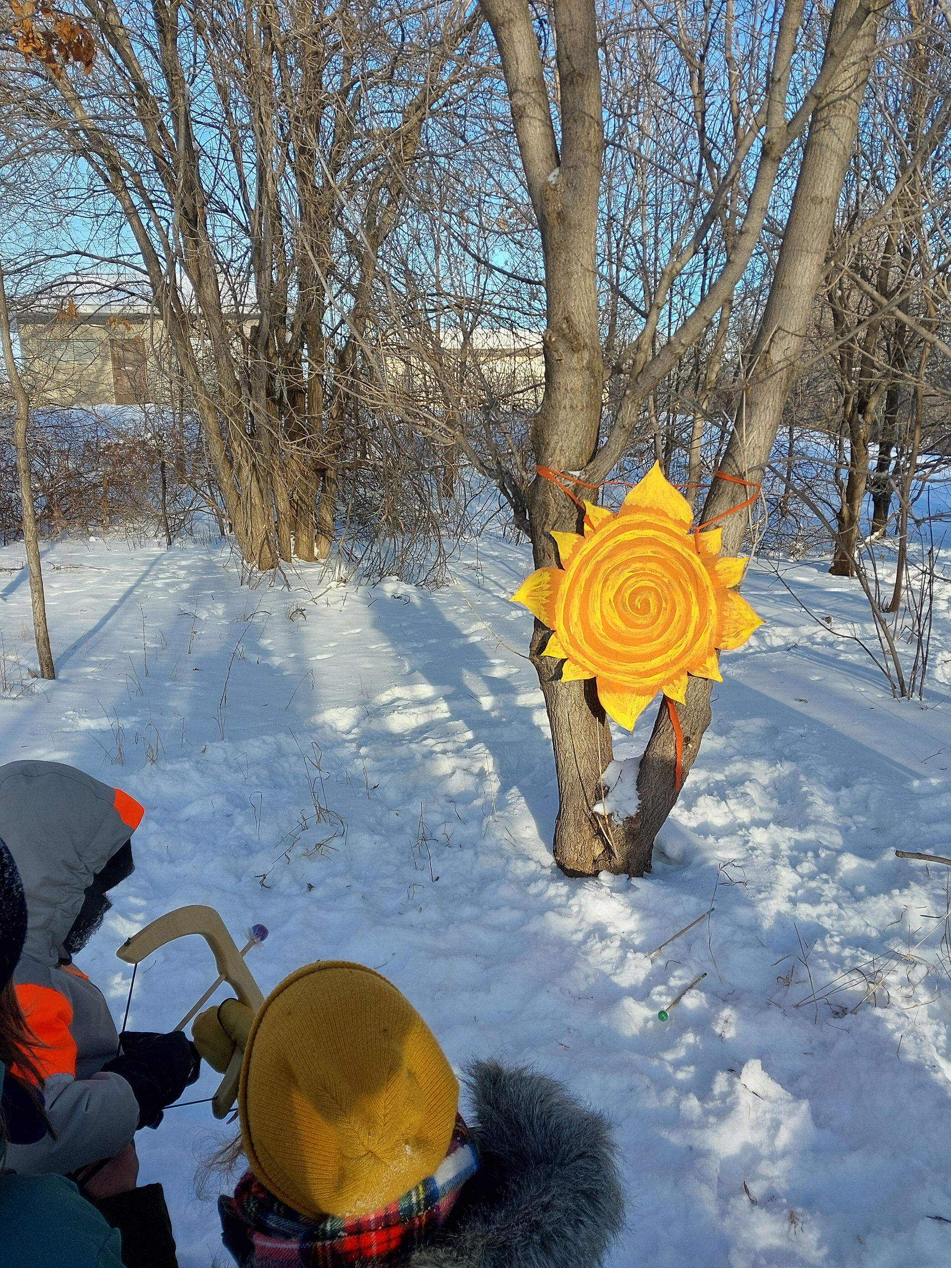A photo on a sunny winter day of a child and educator preparing a small play bow and arrow to shoot at a painted sun