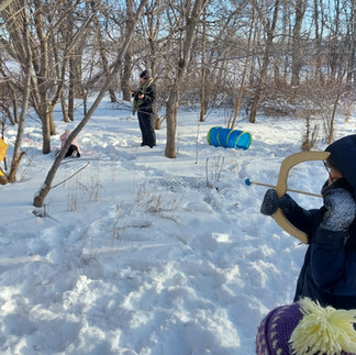 A photo on a sunny winter day of a child with small play bow and arrow ready to shoot at a painted sun. There is also an obstacle course in the background.