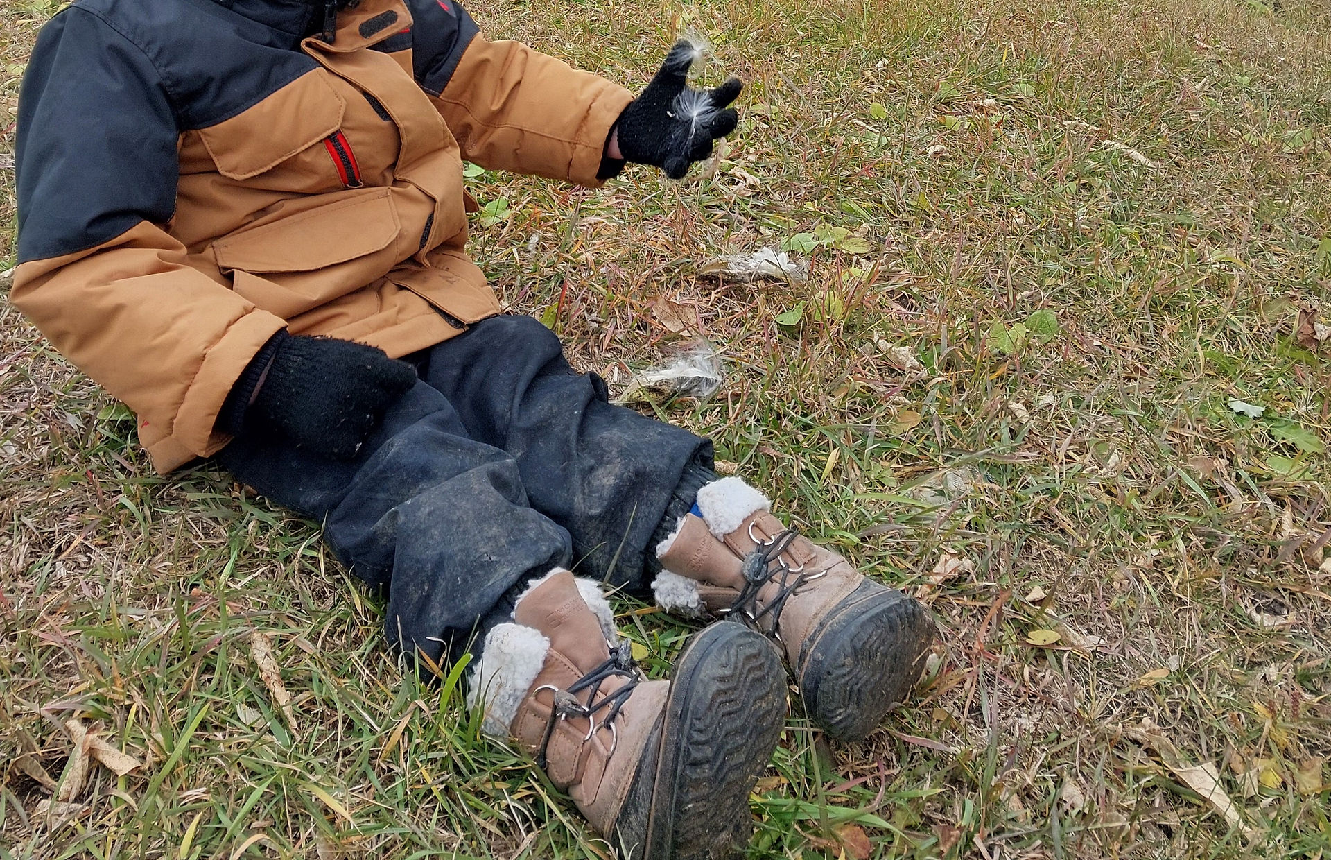 A child sitting outside on the ground holding milkweed seeds