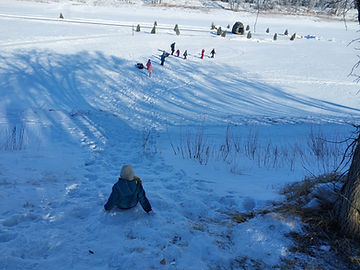 A child sits alone on a hill watching seven other children walk across a frozen river