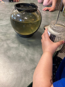 A photo of a child's hands holding a honey jar in front of a tea pot filled with light green nettle tea