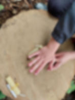Photo of a tree stump that a child is using to role wax into a small candle 