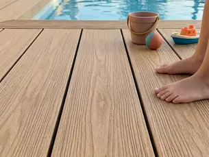 Pies de un niño junto a una piscina, con cubo, pelota y barquito de juguete; patio de madera y ambiente tranquilo.