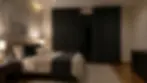 Dormitorio acogedor con cama doble, colchas grises, lámparas de noche encendidas. Cortinas oscuras y cuadro abstracto en la pared.