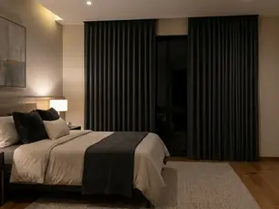 Dormitorio acogedor con cama doble, colchas grises, lámparas de noche encendidas. Cortinas oscuras y cuadro abstracto en la pared.