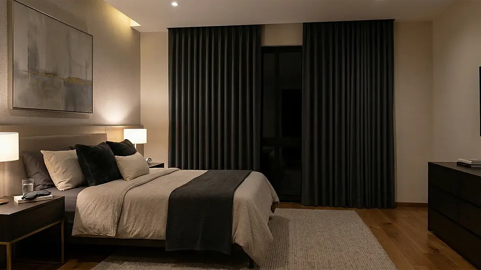 Dormitorio acogedor con cama doble, colchas grises, lámparas de noche encendidas. Cortinas oscuras y cuadro abstracto en la pared.