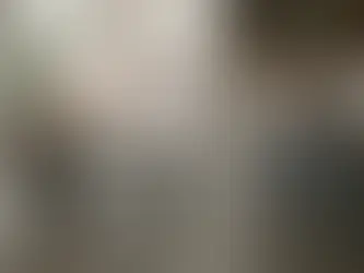 Persona leyendo en una cafetería moderna con suéter marrón, mientras una barista prepara café. Ambiente acogedor y decoración minimalista.