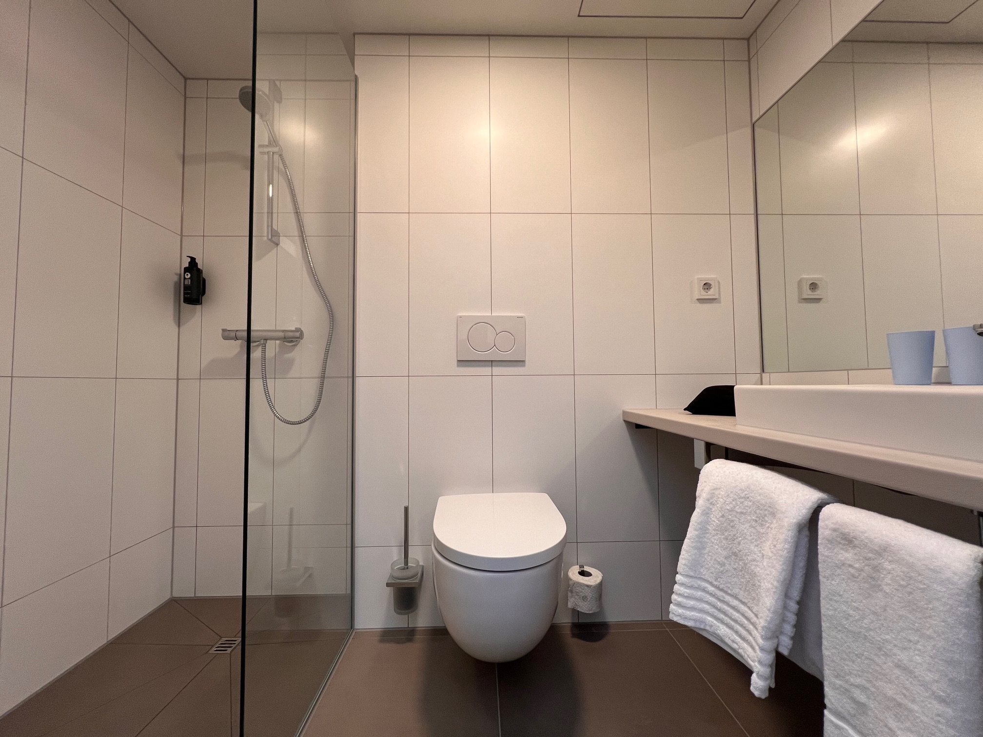 Fertiges Hotelbad mit bodengleicher Dusche, Glastrennwand, WC und Waschtisch im Flughafenhotel Wien