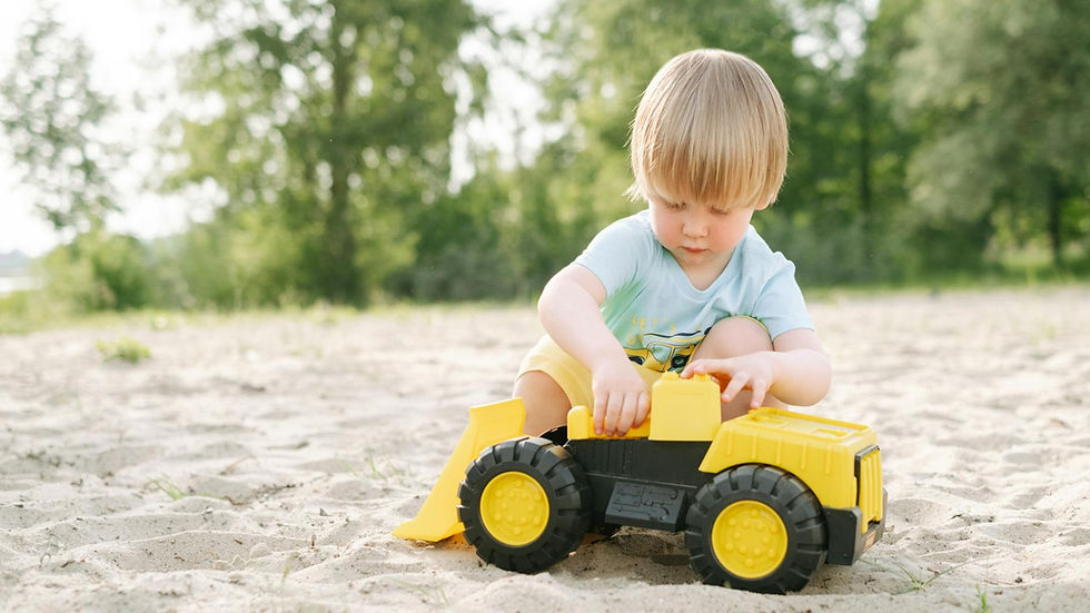 Blonde child enjoys outdoor playtime in a sandy environment with a colorful toy truck.