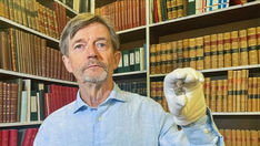 Livros Vikings | Peter Pentz, curador do Museu Nacional da Dinamarca, segura uma peça de tabuleiro primorosamente esculpida. O artefato pode ser a representação mais detalhada de um viking já encontrada. — Crédito da Imagem: Swiss Info