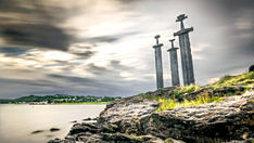 Livros Vikings | Três imponentes espadas de bronze cravadas em uma colina rochosa à beira-mar na Noruega, erguidas como o monumento Sverd i fjell para simbolizar a paz e a unificação após o histórico confronto viking. — Crédito da Imagem: Giuseppe Milo / CC BY 3.0.