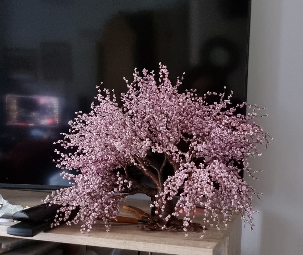 A pink blossom bead and wire tree sculpture sitting on my tv unit in front of my tv. It's a large and very full of detail tree with hundreds of branches in clouds of pink beads