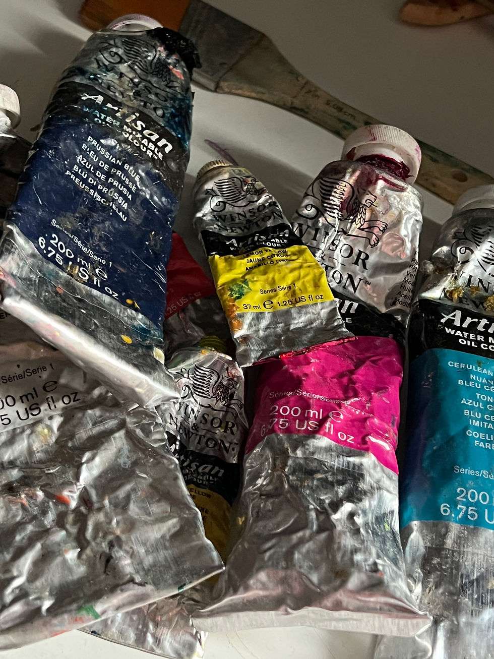 Crumpled tubes of Winsor & Newton artist oil paint in blue, yellow, pink and teal on a shelf.