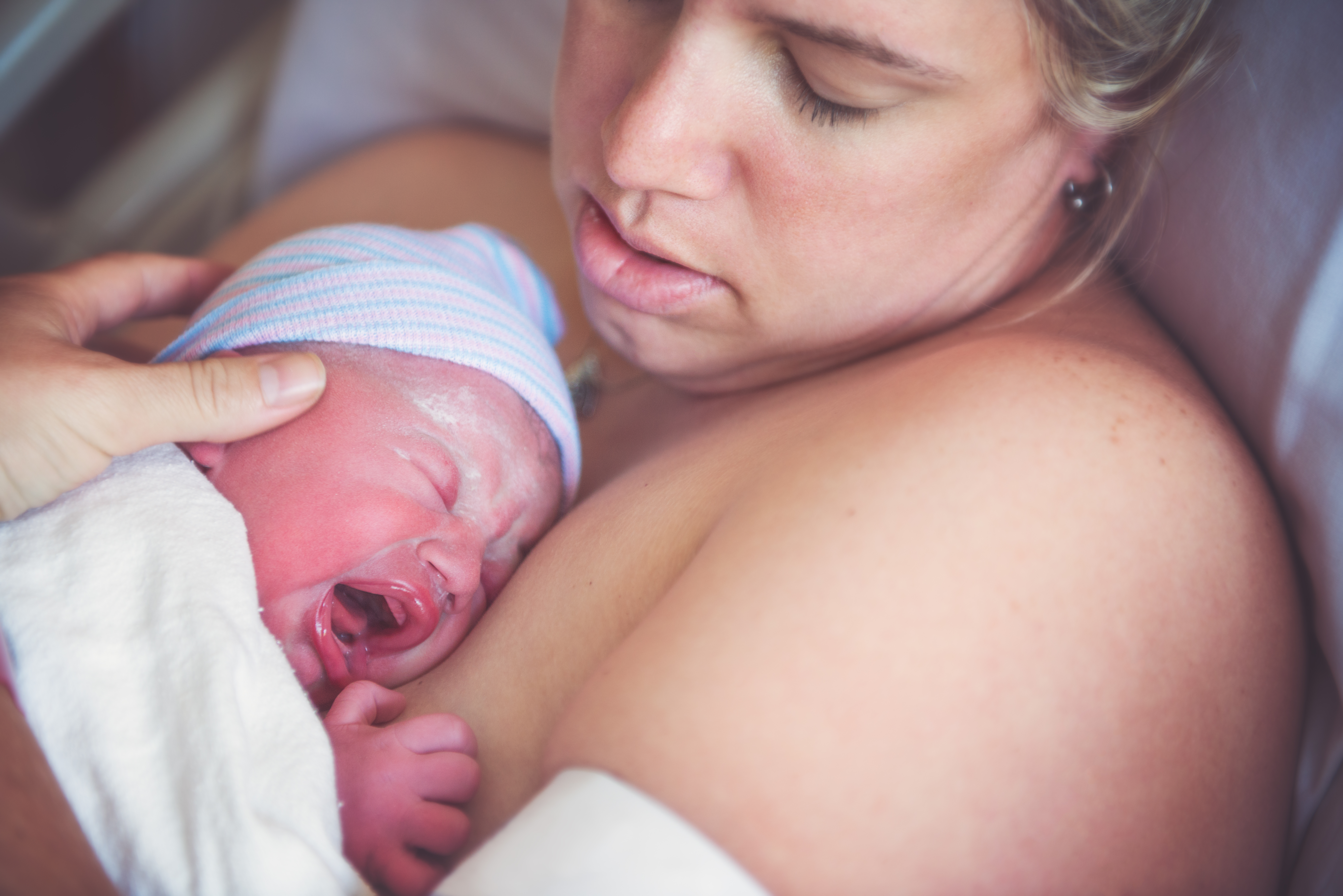 a mother holds a crying newborn baby on her chest