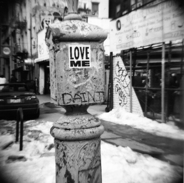 Black and white image of an Alarm box with a sticker that says Love Me in winter in New York. Shot on film and printed in the darkroom
