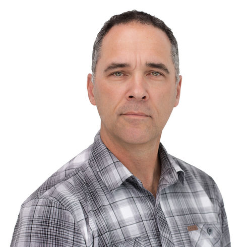 Seattle studio headshot of a man with short graying hair in a gray plaid button-up shirt, neutral confident expression, white background.