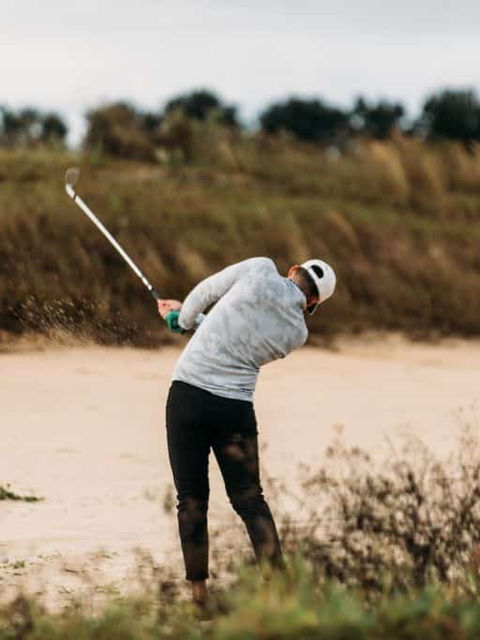 a man swinging a golf club on top of a sandy beach