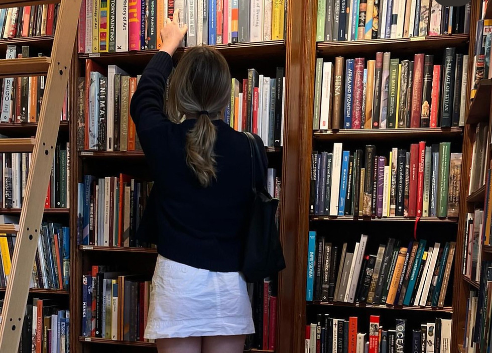 Olivia, turned away picking a book out from a library shelf.