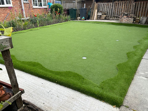 a man in a blue shirt stands in front of a putting green