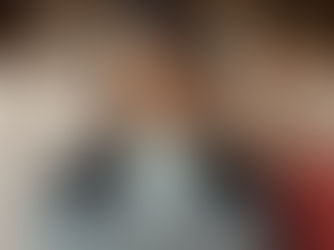 Smiling woman in glasses using a laptop on a beige sofa, with a bookshelf and plants in the background. Cozy and focused atmosphere.