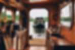 Cozy houseboat interior with wooden decor and kitchenware. A green boat is visible through the open door, floating on a calm river.