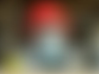 Construction worker in a red hard hat and mask in a building site, wearing a safety vest. Background shows metal beams and a dimly lit area.