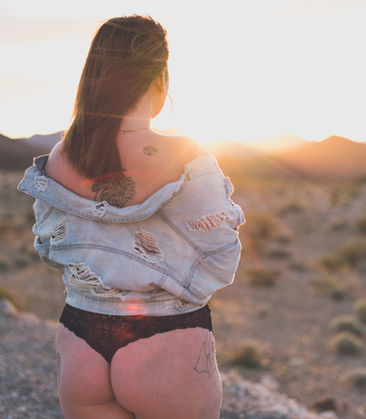 Woman in denim jacket, desert landscape, sunset background.